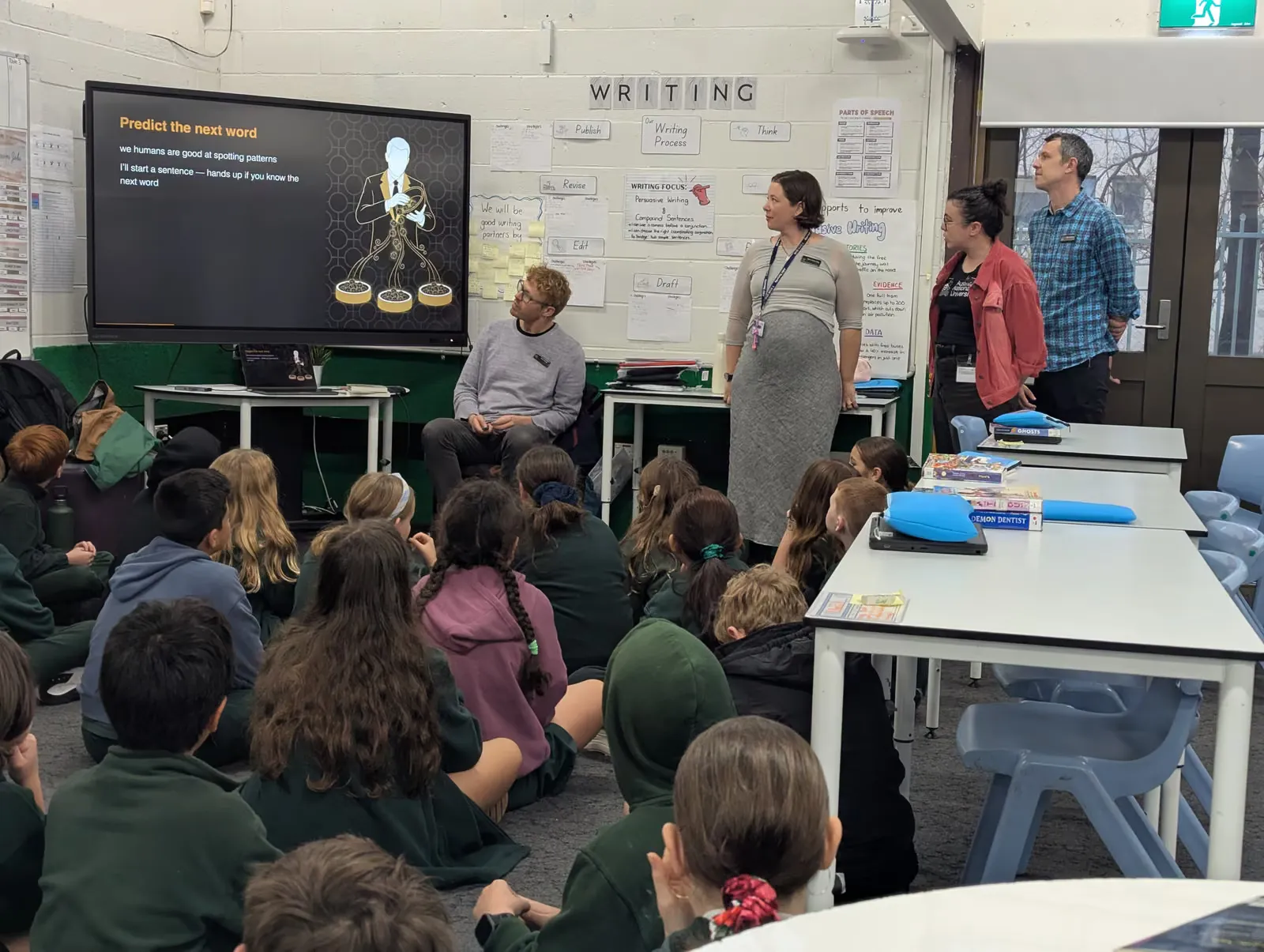 Duffy Primary Year 5 students seated facing the front of the room as two facilitators present a slide headed "Writing"