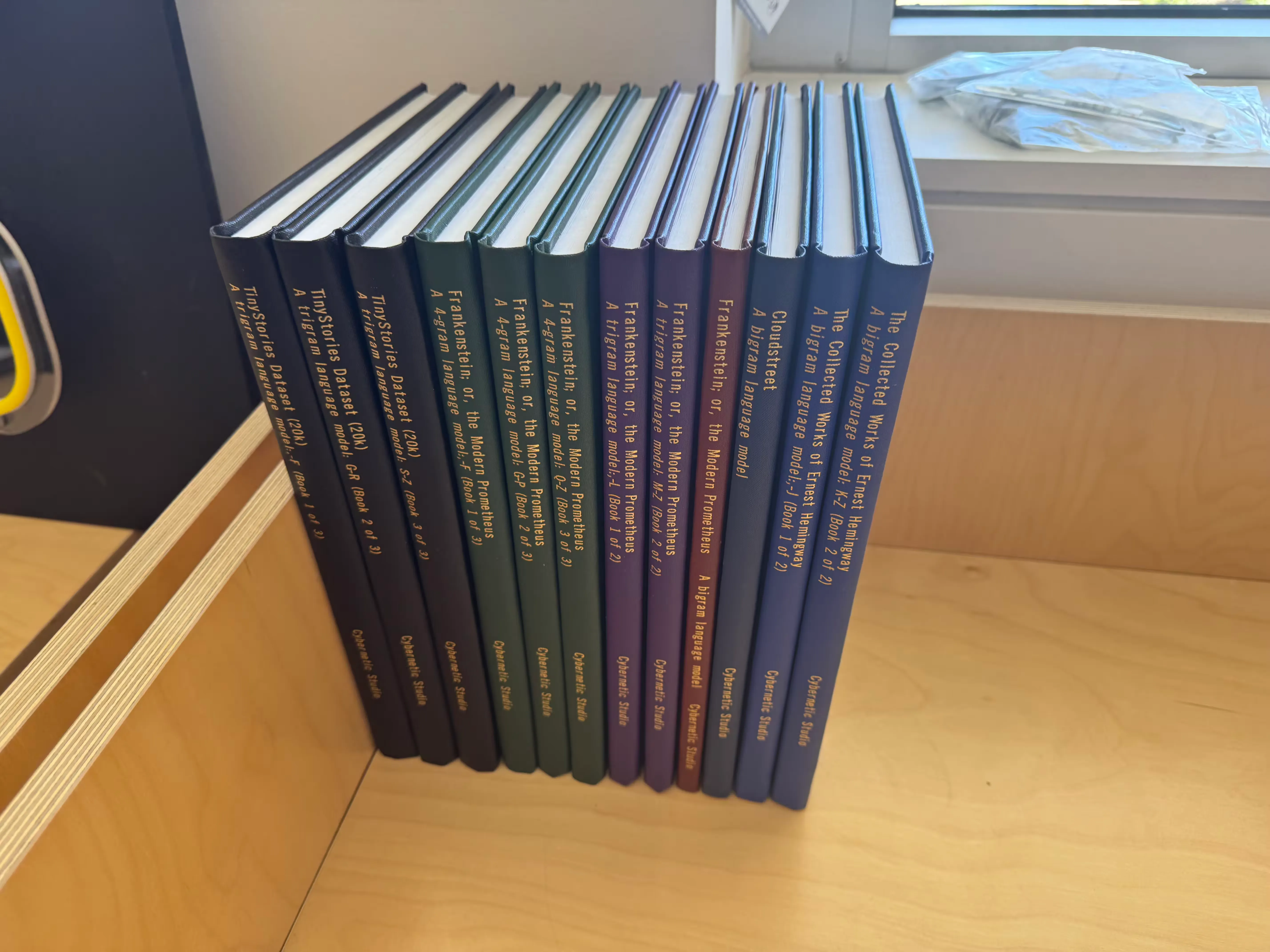 The LLMs Unplugged Library collection — hardbound volumes in green, purple, brown, and blue lined up on a shelf