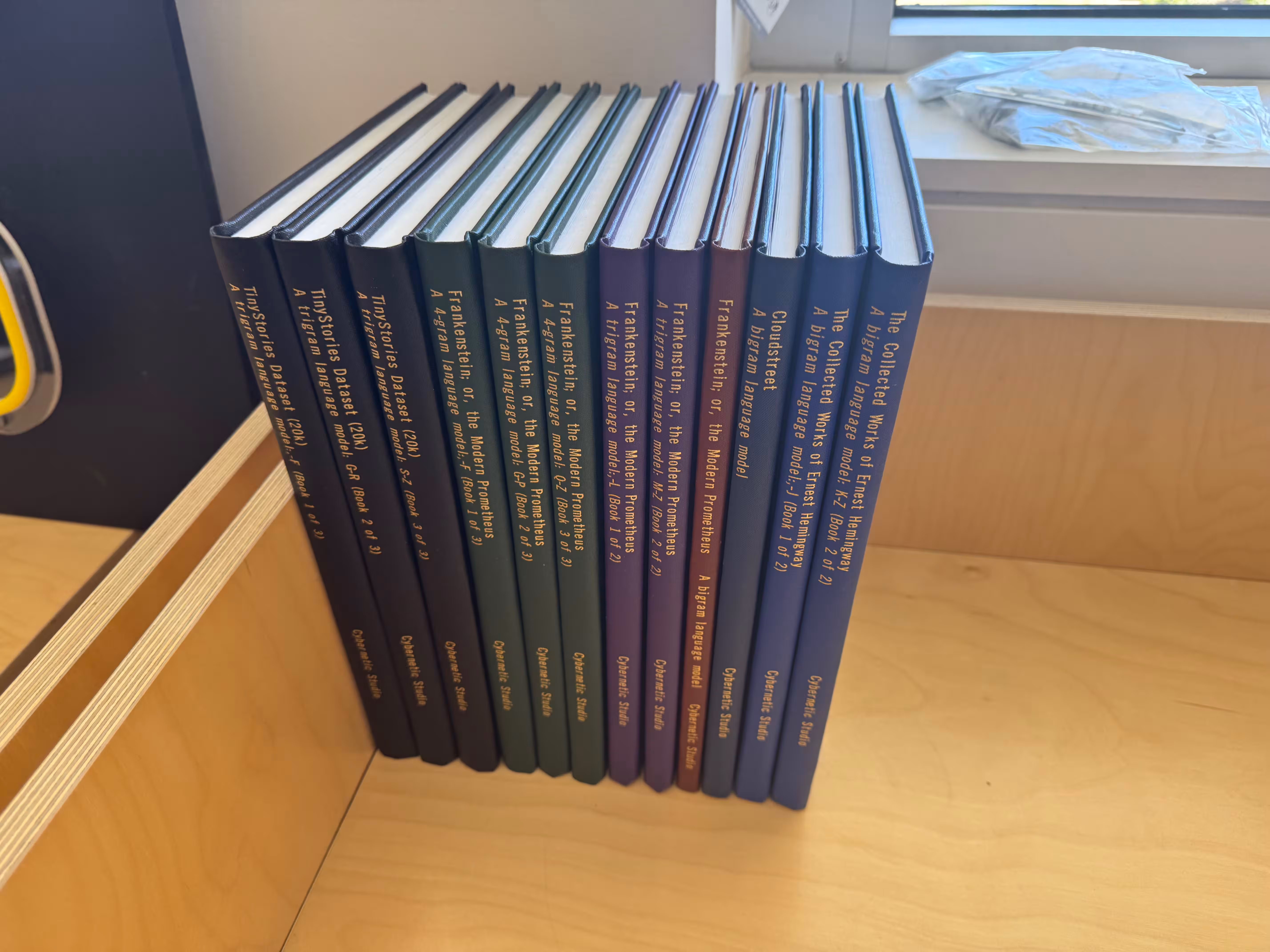 The LLMs Unplugged Library collection — hardbound volumes in green, purple, brown, and blue lined up on a shelf