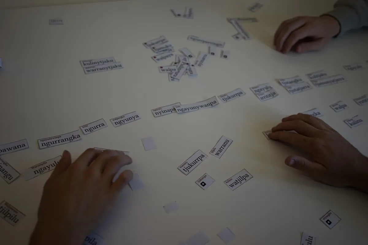 Hands arranging Luritja word tokens: ngurra, ngayulu, tjukurrpa, warranu, nyinapa, ngayunywanpa